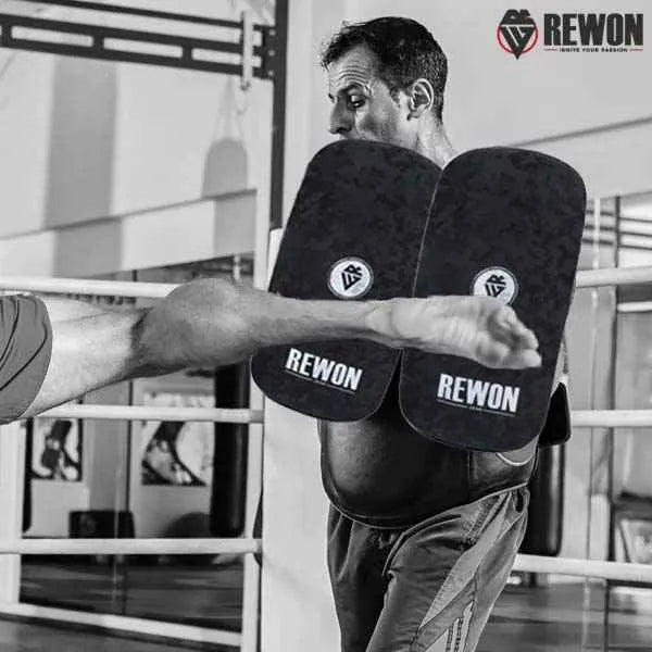 Trainer using Rewon camouflage MMA kick pads during boxing or martial arts session in a gym setting.
